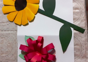 „Wiosenne kwiaty". Praca przedstawia dwa kolorowe kwiaty wykonane metodą origami. Na dole różowy kwiatek wykonany z cienkich pasków papieru. Powyżej widać kwiat, którego Lena wykonała z żółtych pozaginanych kółek, z zielonego papieru zrobiła łodygę i liście.